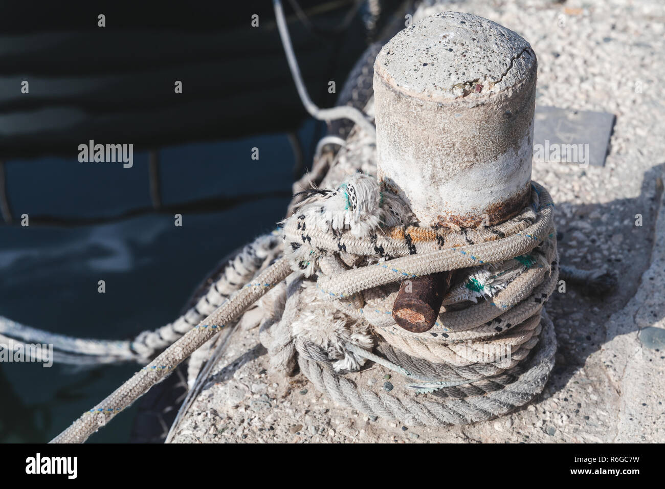 Liegeplatz Poller mit gebunden naval Seile steht auf konkrete Pier im Hafen, Nahaufnahme Stockfoto