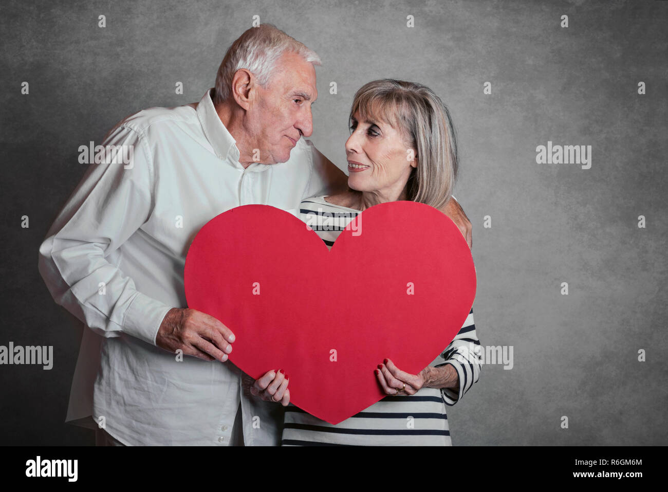 Portrait von Happy senior Paar mit einem roten Herzen auf grauem Hintergrund Stockfoto