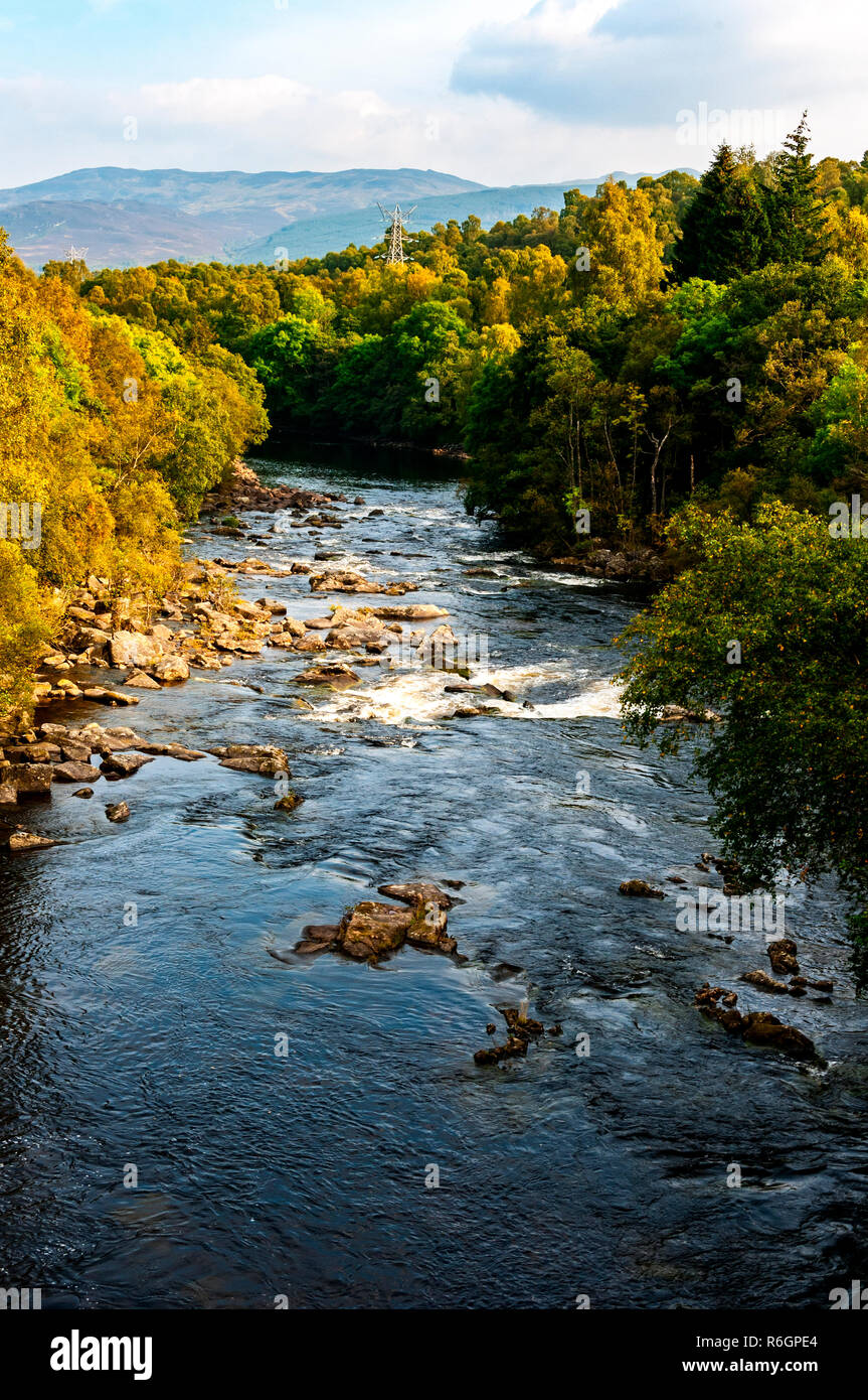 Der Fluss Tummel würdevoll fließt zwischen Banken mit majestätischen Bäumen bedeckt, einige bereits Braun im Herbst Sonnenschein, auf dem Weg zu fernen dunstige Berge Stockfoto