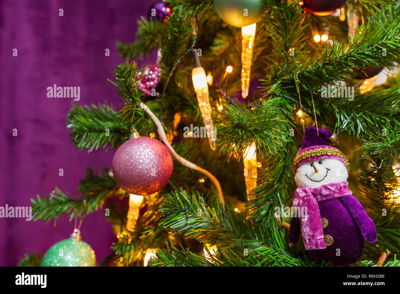 Weihnachtsbaum in einem lila Thema mit einem prominenten lila Schneemann und dekorative lila Bälle und Kerzenlicht in Sicht eingerichtet Stockfoto