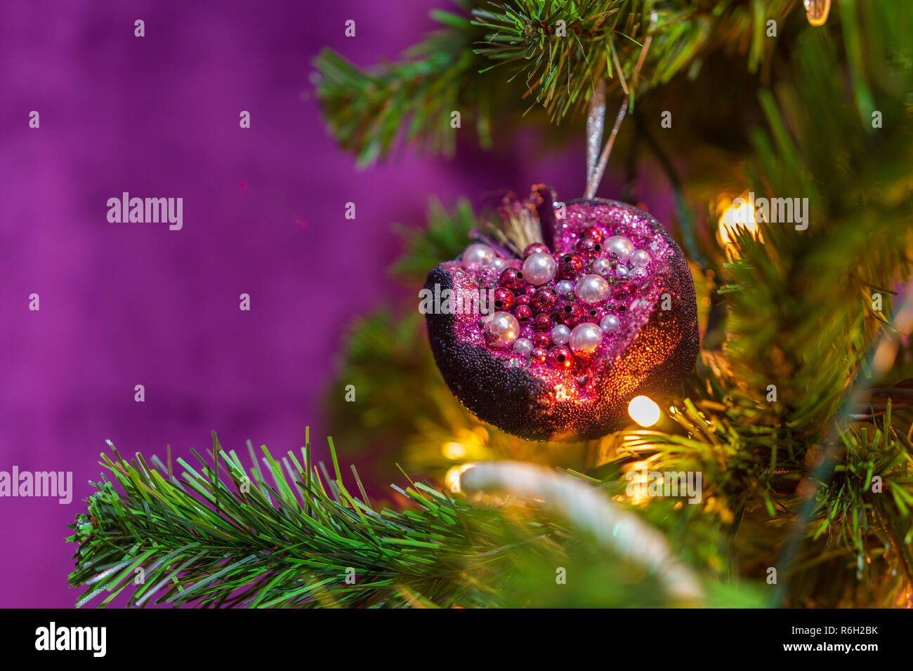 Nahaufnahme einer Weihnachtsbaum in einem lila Thema mit einem prominenten lila Granatapfel hängende Dekoration in Sicht eingerichtet Stockfoto