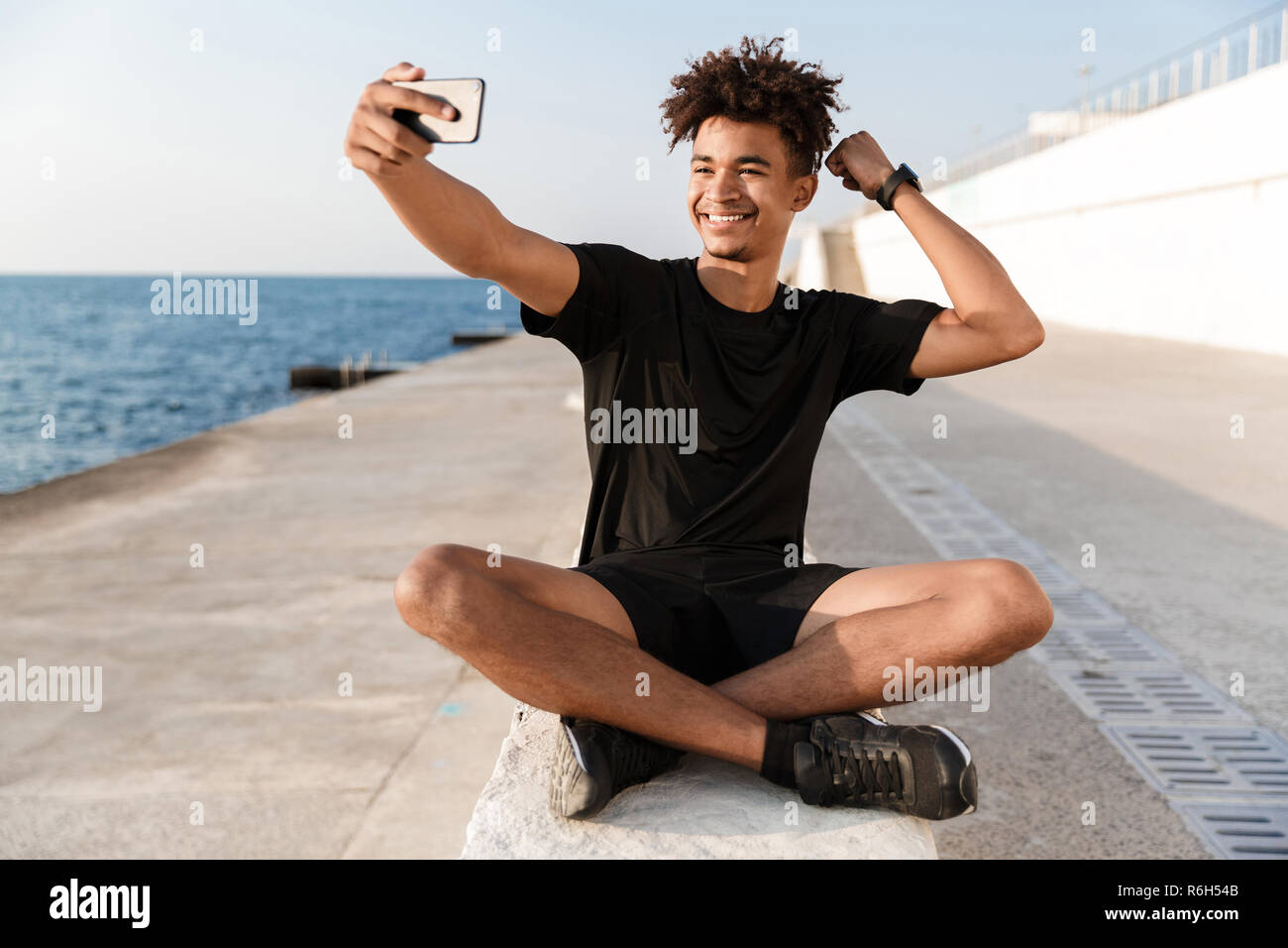 Glückliche junge afrikanische Sportler am Strand unter einem selfie, flexing Biceps Stockfoto