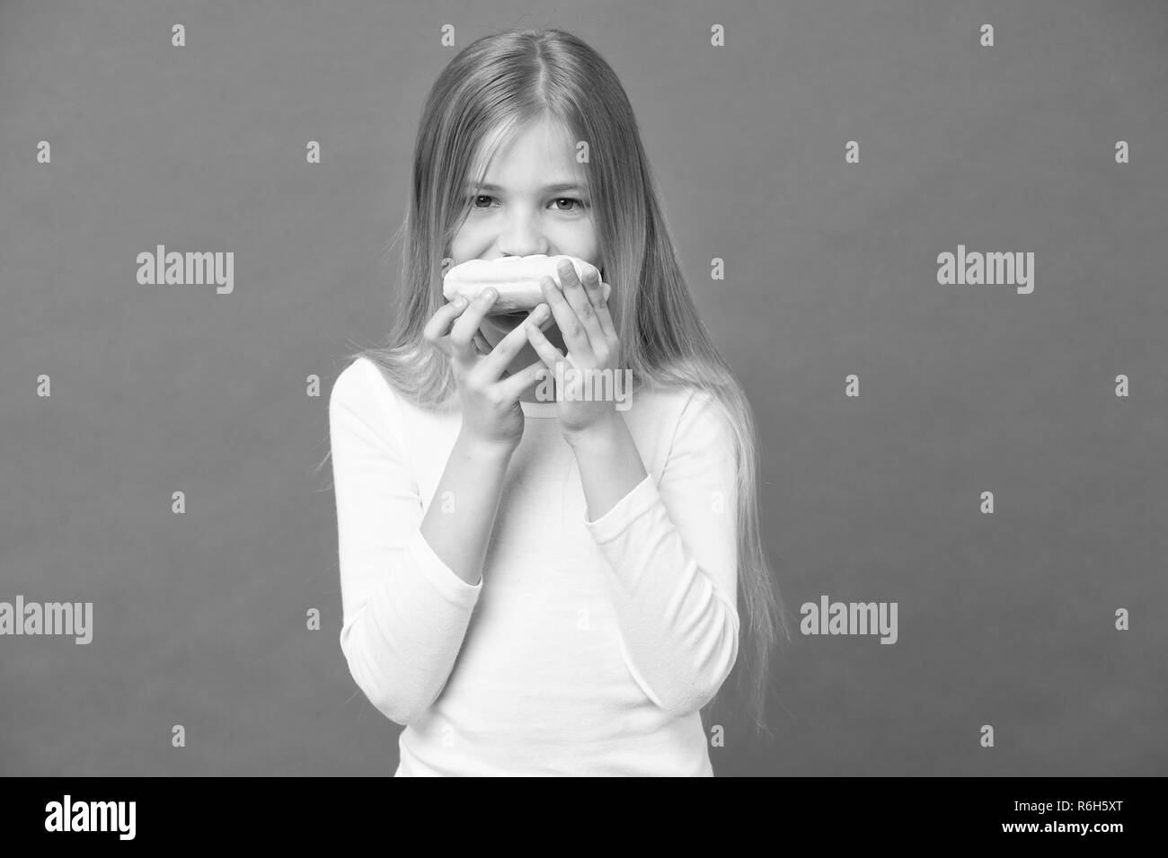 In Snacks. Kind essen Donut auf Violett Hintergrund. Kleines Mädchen mit glasierten ring Donut auf lila Hintergrund. Kind mit Junk Food. Essen für Snacks und Dessert. Kindheit und Kinderbetreuung, kopieren. Stockfoto