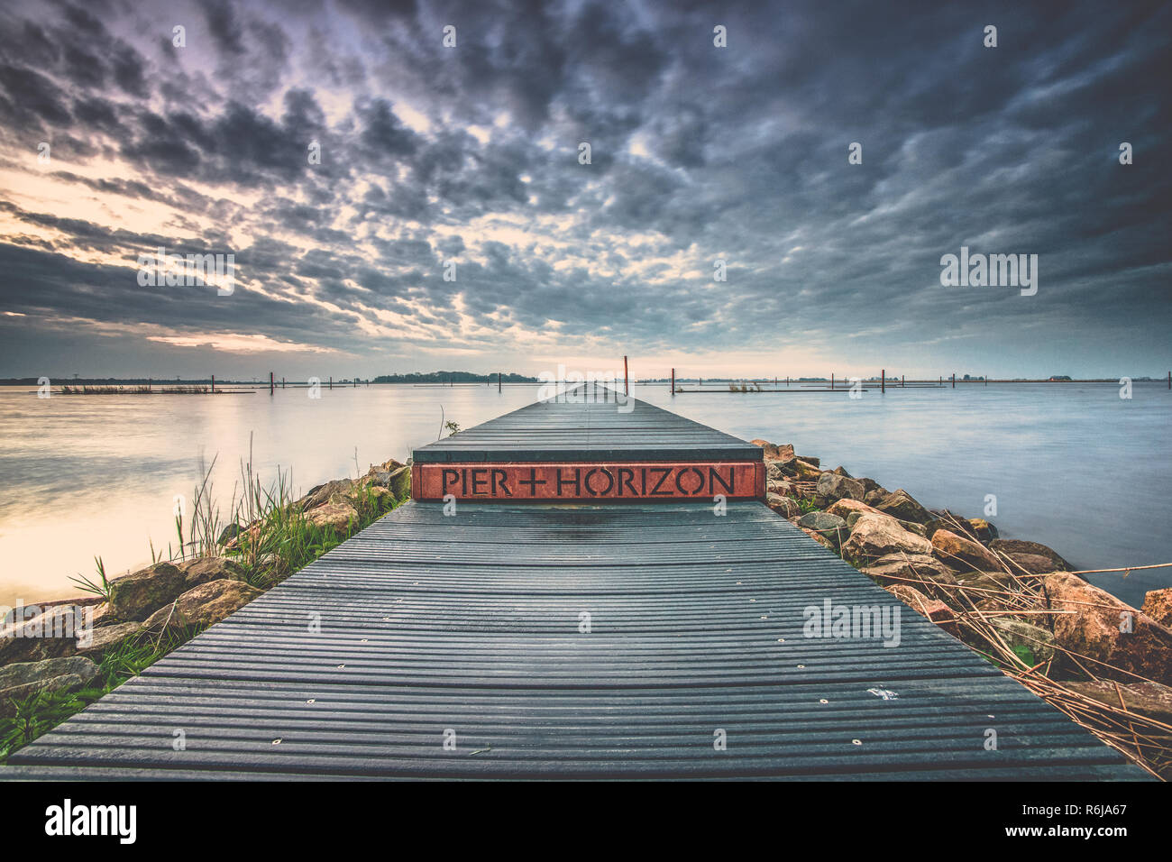 Landart in den Niederlanden. Vista mit Wasser, Steg und Natur unter einem schönen bewölkten Himmel mit sunrise Farben und Kontrast. Stockfoto