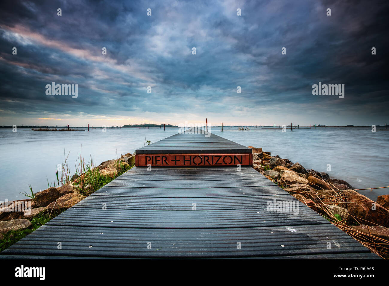 Landart in den Niederlanden. Vista mit Wasser, Steg und Natur unter einem schönen bewölkten Himmel mit sunrise Farben und Kontrast. Stockfoto