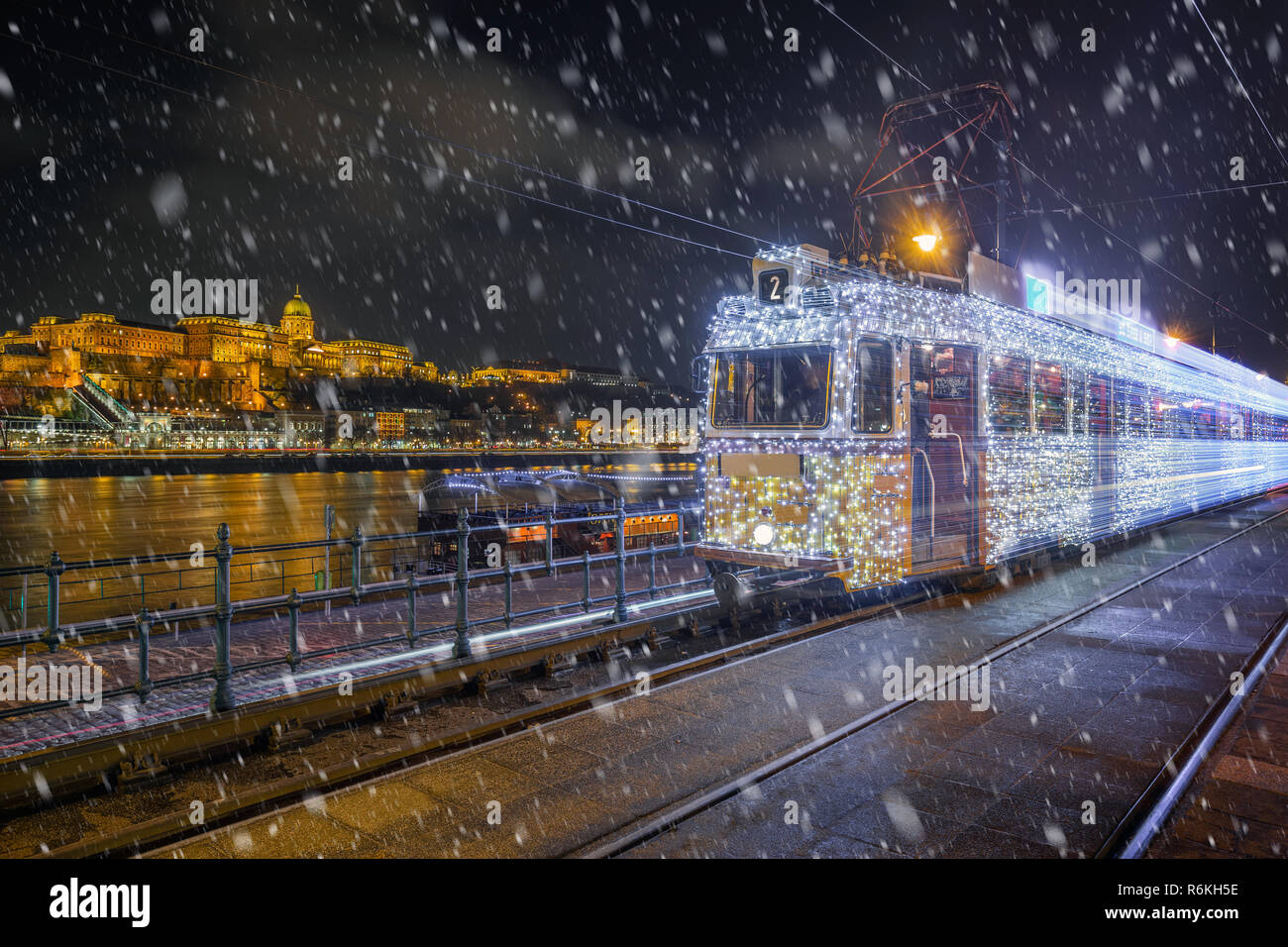 Budapest, Ungarn - festlich geschmückten Licht Straßenbahn (fenyvillamos) unterwegs mit Buda Castle Royal Palace at Vigado Quadrat auf einer verschneiten Nacht Stockfoto