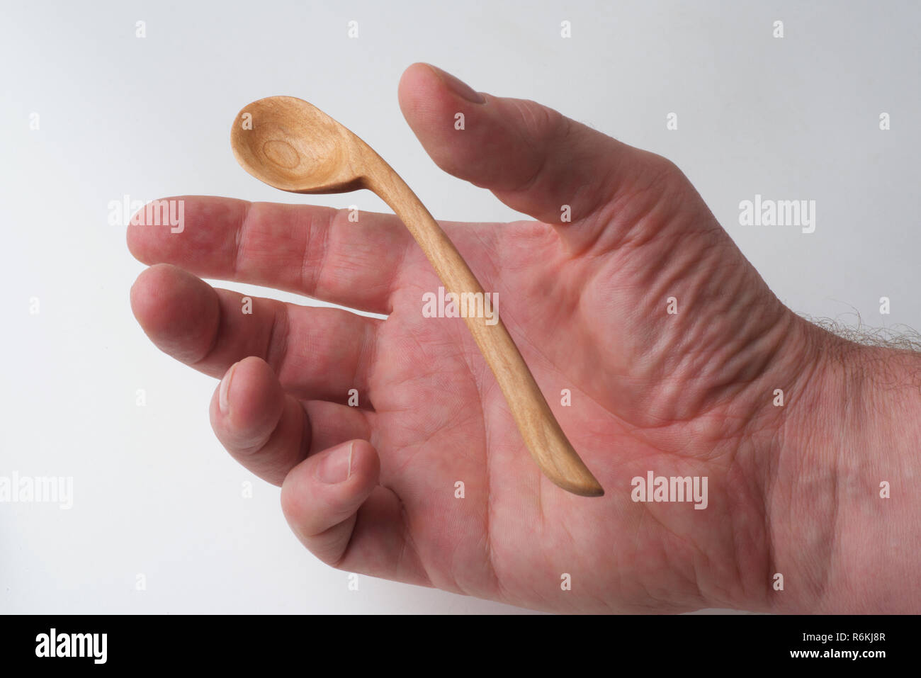 Eine männliche Hand erreicht eine handgefertigte Holzlöffel zu erfassen, auf einem weißen Hintergrund. Stockfoto