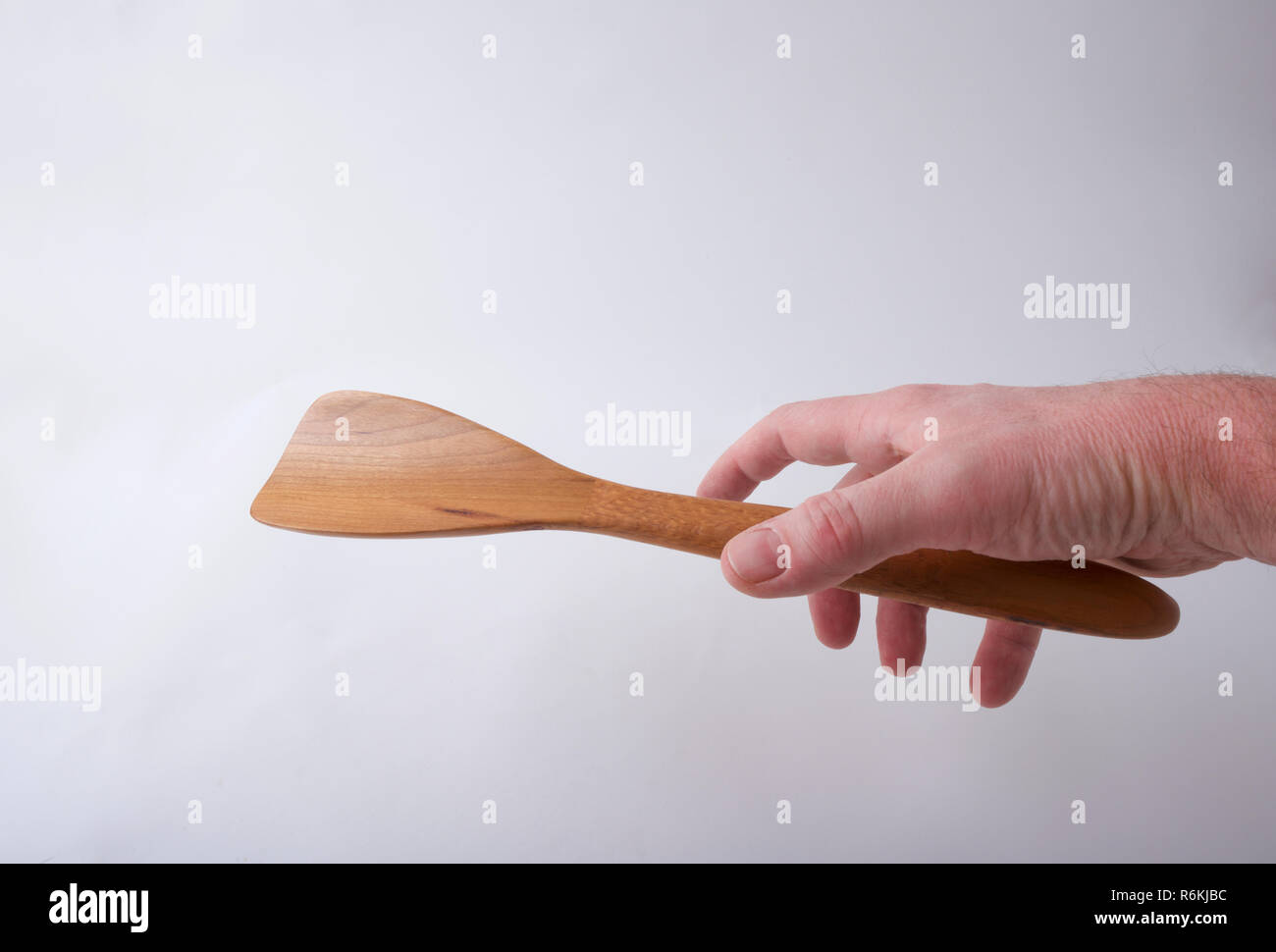Eine männliche Hand erreicht eine handgefertigte Holzspachtel zu erfassen, auf einem weißen Hintergrund. Stockfoto