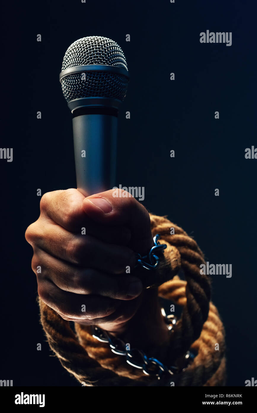 Die Freiheit der Presse und Journalismus, konzeptionelle Bild mit Mikrofon in männlicher Hand mit Ketten und Seile, Low Key Image gebunden Stockfoto
