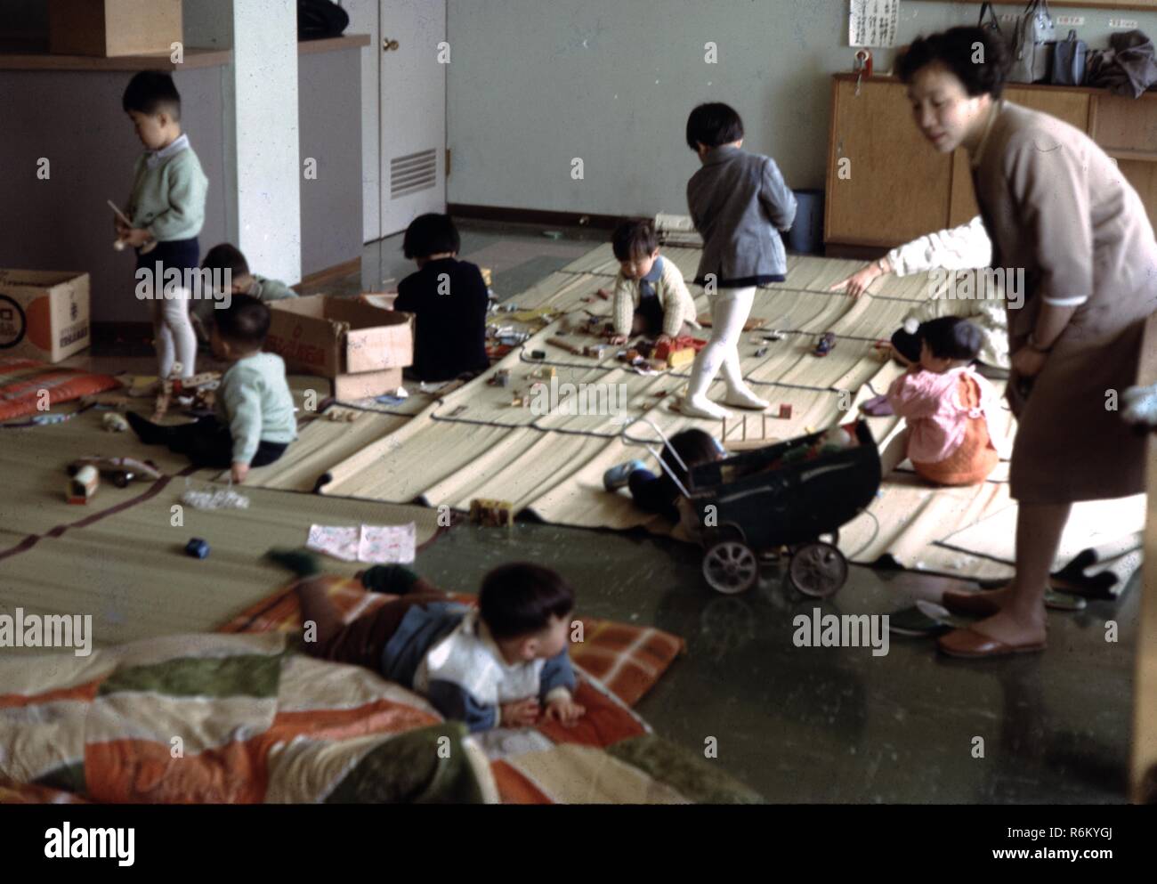 Eine Frau Uhren mehrere Kinder, die auf den traditionellen Bambus Matts spielen, in eine Vorschule Unterricht an einer christlichen missionarischen Kirche in der Nachkriegszeit in Japan, 1961. () Stockfoto