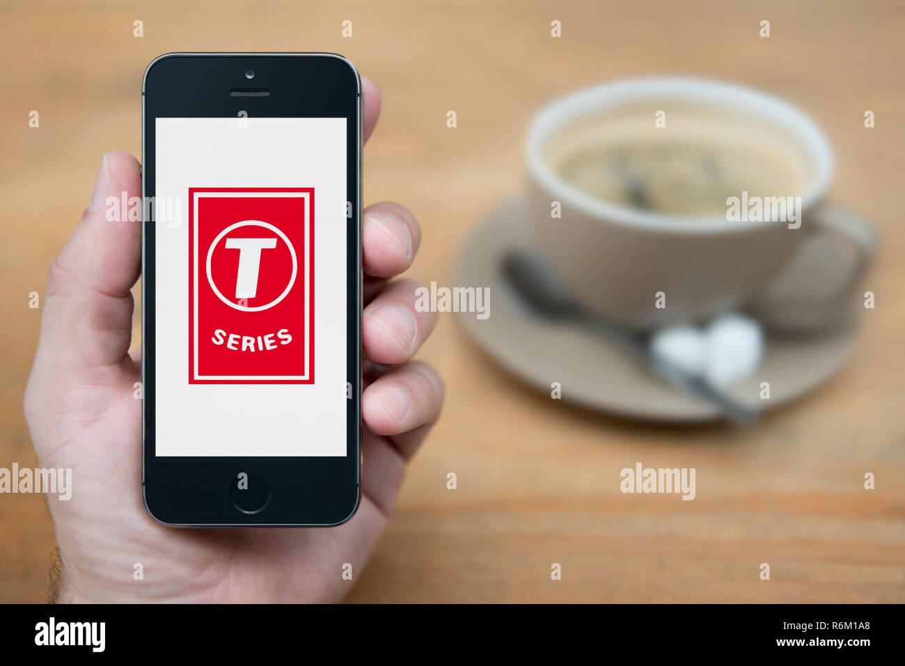 Ein Mann schaut auf seinem iPhone die zeigt die T-Serie Logo (nur redaktionelle Nutzung). Stockfoto