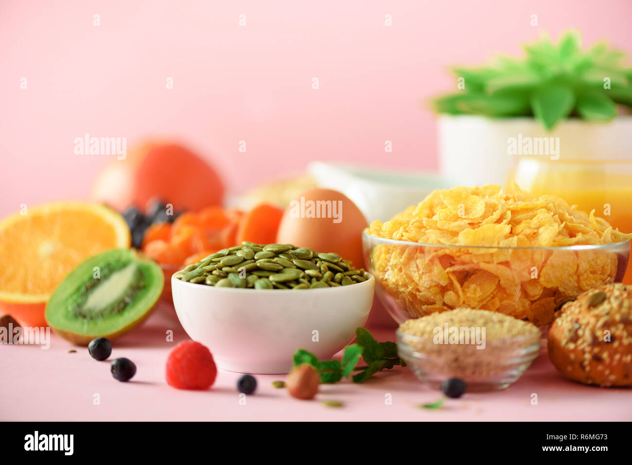 Cornflakes mit Milch, Kürbiskerne, frische Beeren, Joghurt, gekochte Eier, Nüsse, Obst, Orange, Banane, Pfirsich für Frühstück auf rosa Hintergrund. Kopieren Sie sp Stockfoto