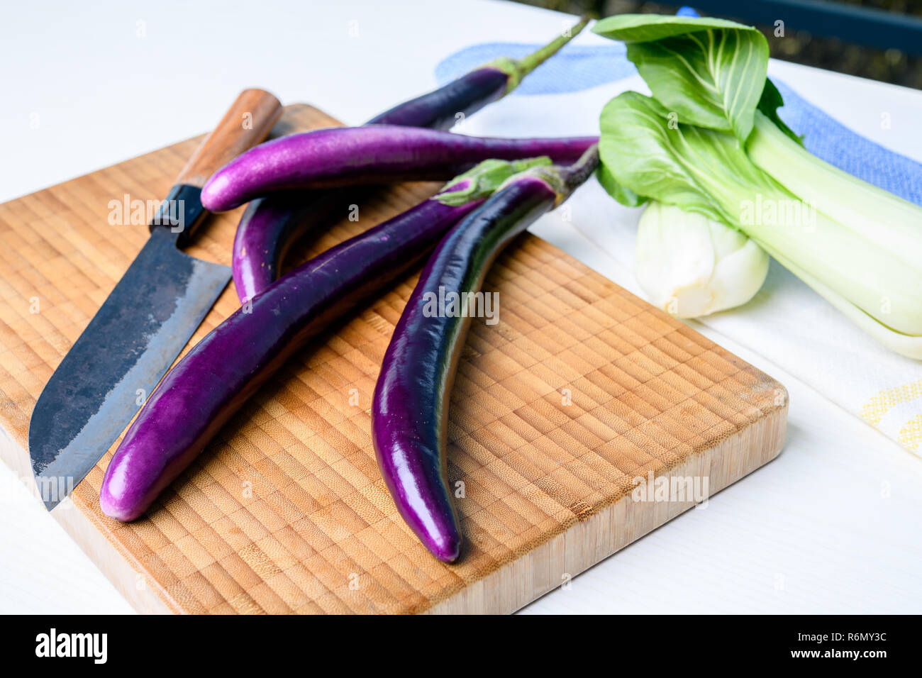 Japanische Aubergine auf Holzbrett mit Messer und Pak Choi Salat Stockfoto