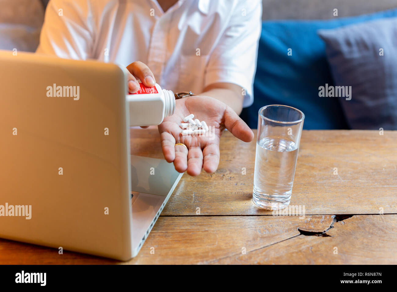 Mann die Pille mit einem Glas Wasser und Laptop auf dem Holztisch. Stockfoto