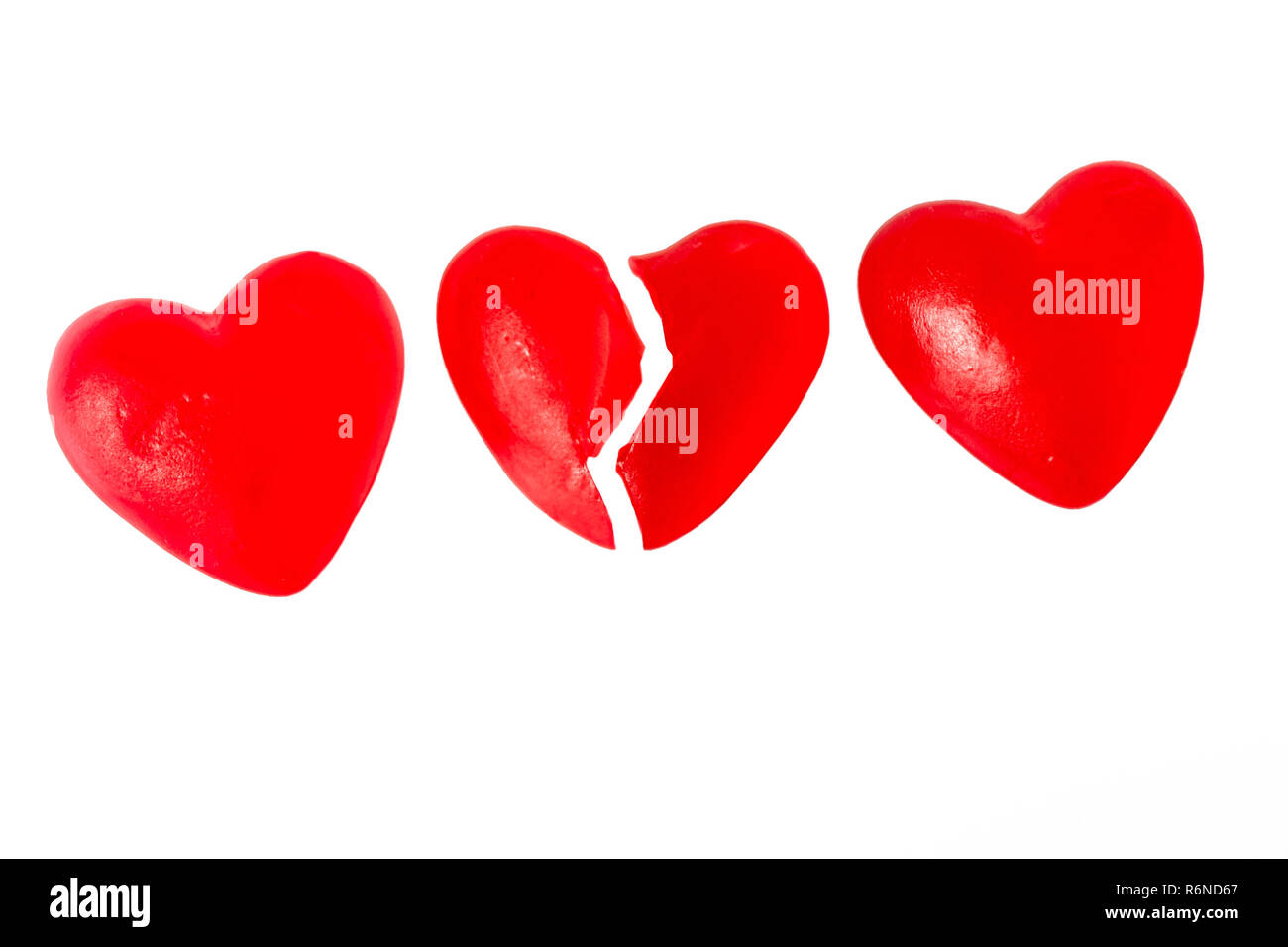 Gebrochene Herzen oder Kummer Konzept mit drei helle rote Gelee Herz geformten Süßigkeiten nebeneinander mit einem Schnitt in der Hälfte auf weißem Hintergrund Stockfoto