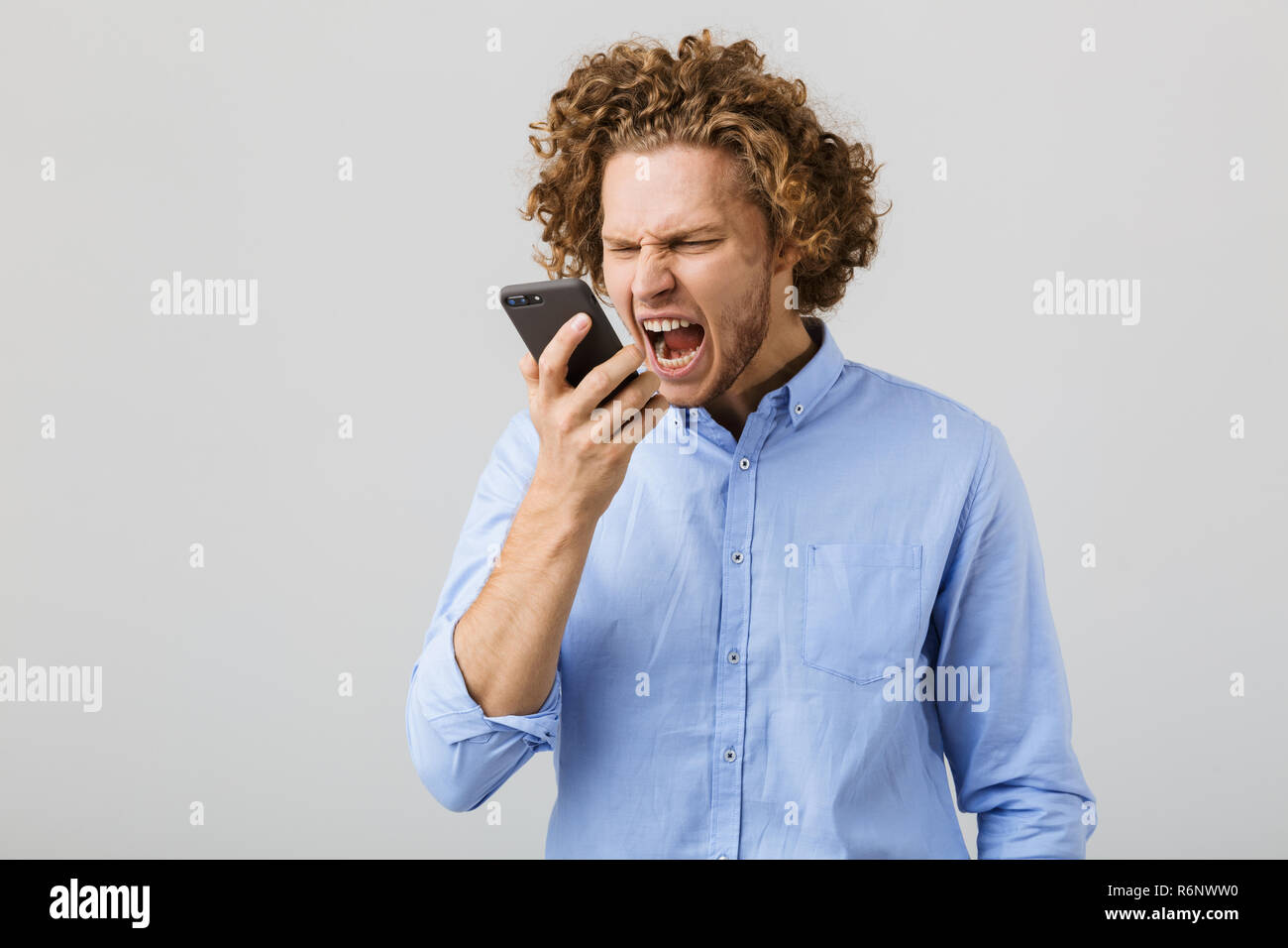 Porträt eines zornigen jungen Mann mit lockigem Haar auf weißem Hintergrund, kreischend an Handy Stockfoto