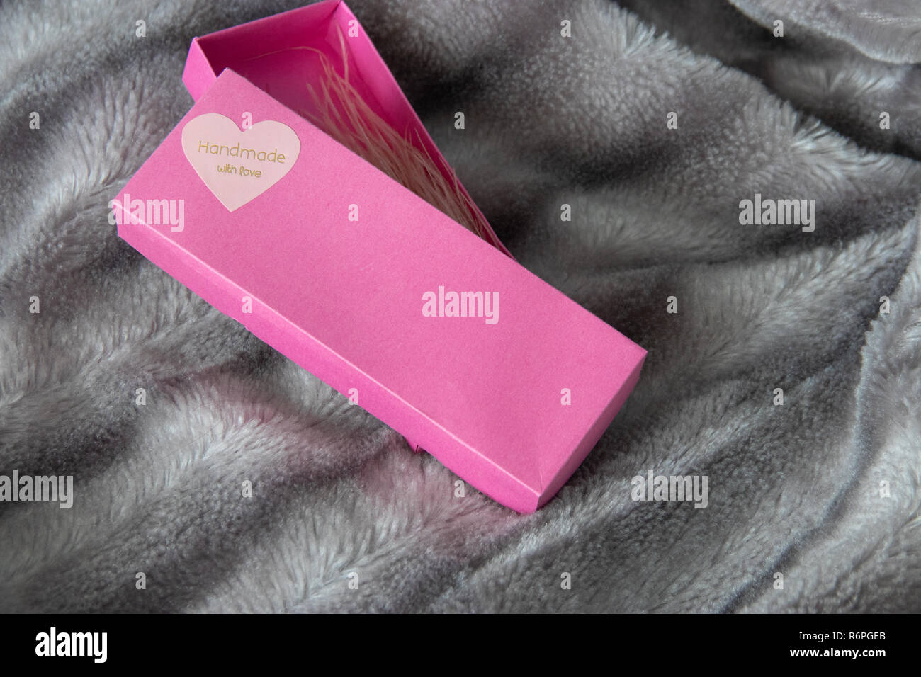 Big Pink Geschenkbox mit einem Herz voller Liebe auf das Silber Grau flauschigen Fellimitat decke Hintergrund geöffnet. Label Handarbeit mit Liebe am Herzen. Straußenfedern Ohrringe in Box Stockfoto