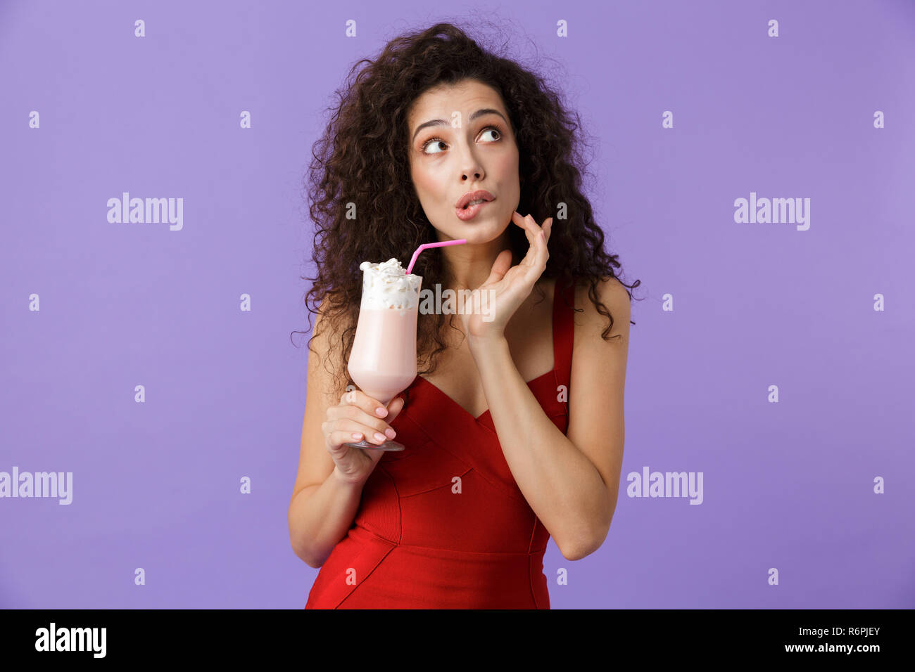 Porträt einer netten Frau mit dunklen lockigen Haar rotes Kleid über violett Hintergrund isoliert, trinken Milch aus einem Glas schütteln Stockfoto