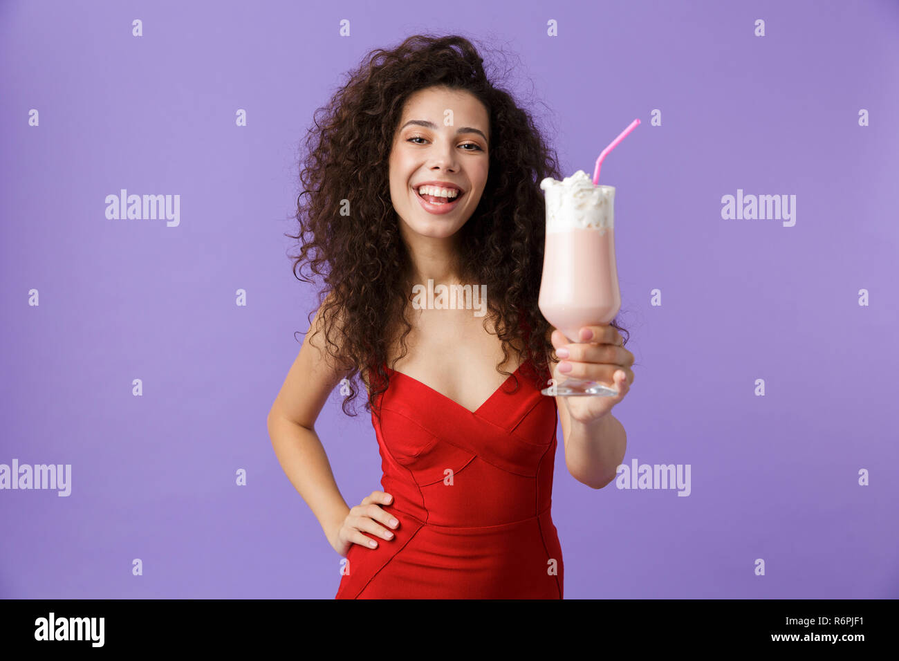 Portrait von freut sich Frau mit dunklen lockigen Haar rotes Kleid über violett Hintergrund isoliert, trinken Milch aus einem Glas schütteln Stockfoto