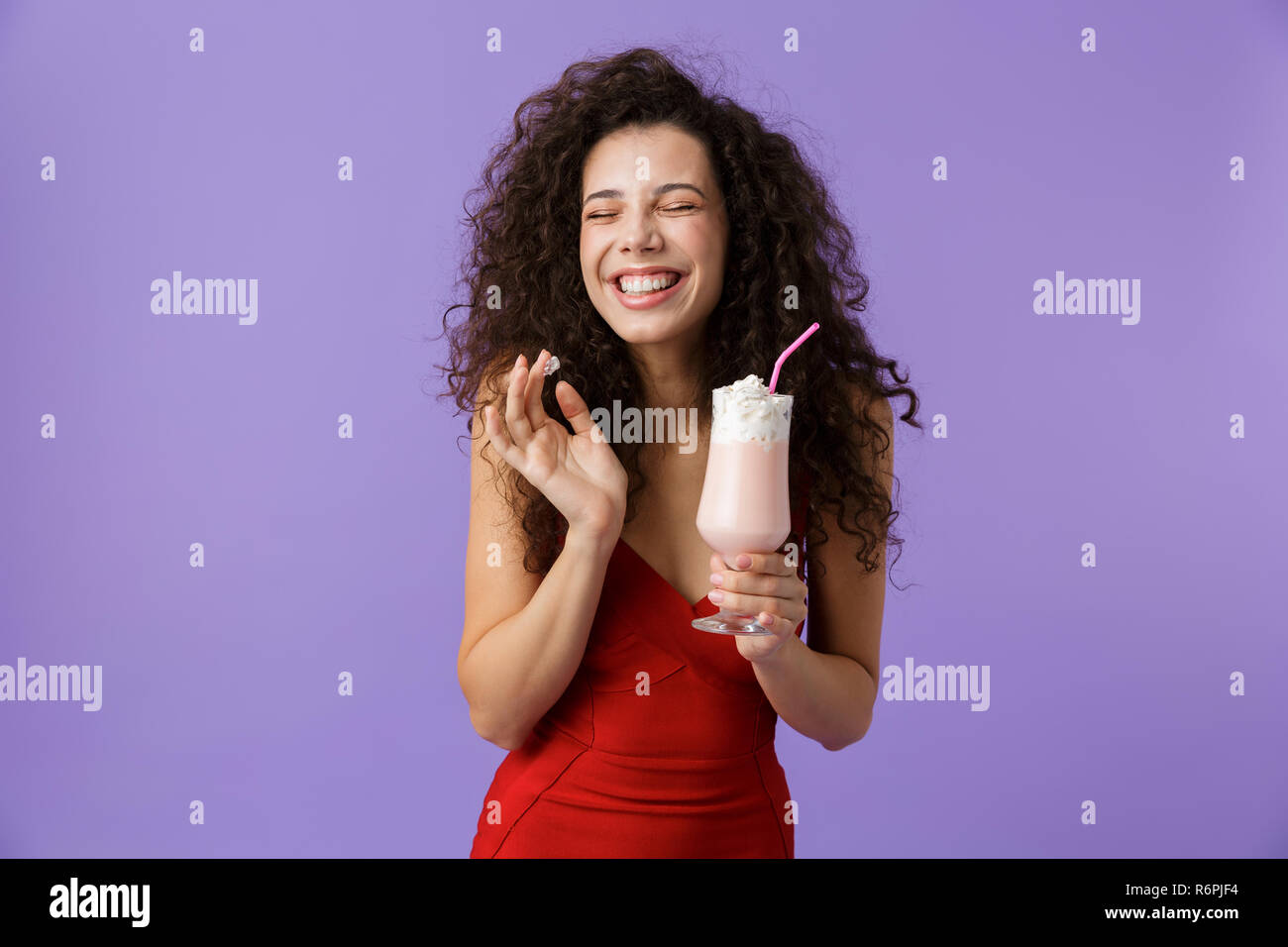 Porträt eines zufriedenen Frau mit dunklen lockigen Haar rotes Kleid über violett Hintergrund isoliert, trinken Milch aus einem Glas schütteln Stockfoto