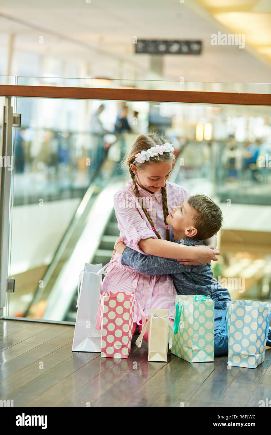 Geschwister zwischen vielen Einkaufstüten halten einander im Einkaufszentrum Stockfoto