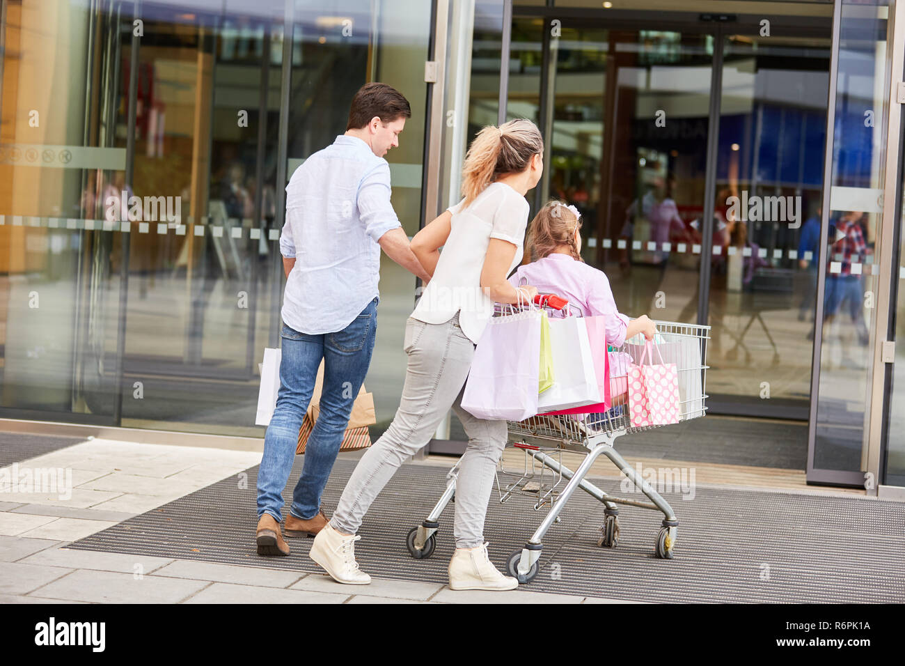 Eltern drücken Kinder in den Warenkorb der Mall Stockfoto