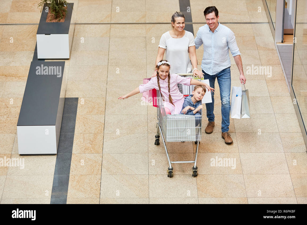 Familie schiebt zwei Kinder im Warenkorb beim Shopping in der Mall Stockfoto