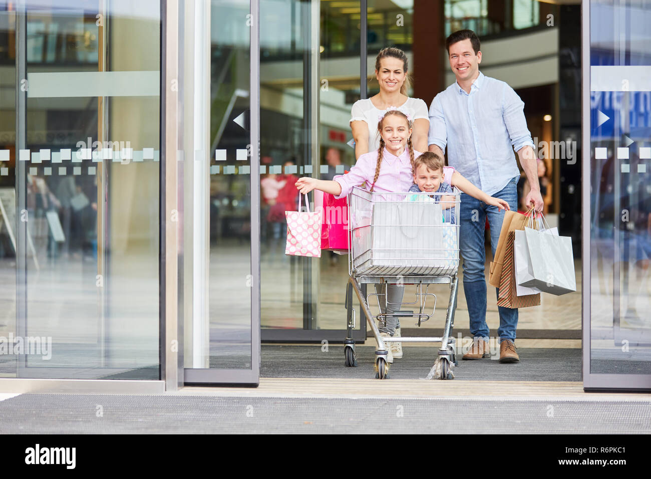 Eltern drücken Kinder im Warenkorb nach dem Shopping in der Mall Stockfoto