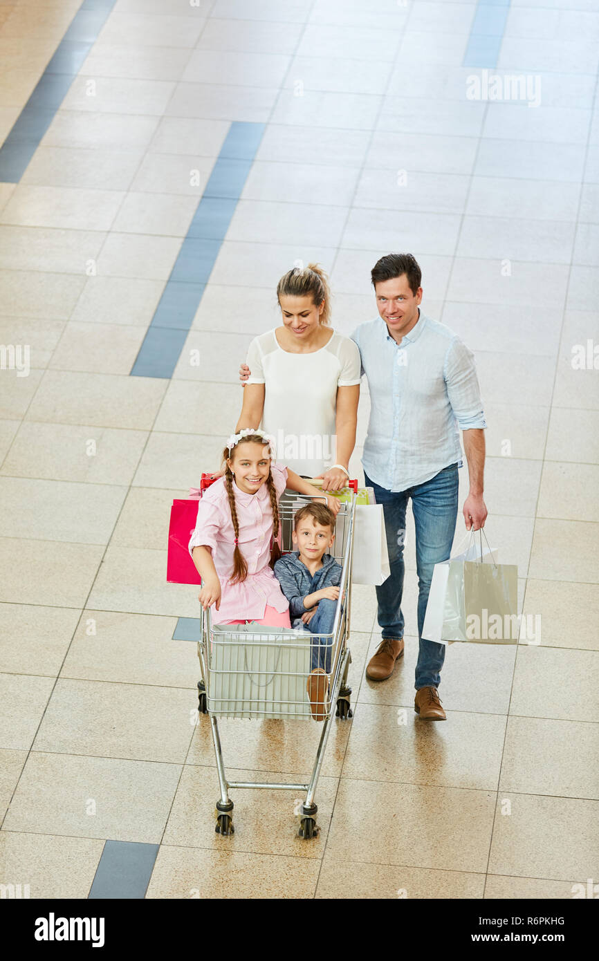 Glückliche Eltern drücken Sie zwei Kinder im Warenkorb durch die Mall Stockfoto