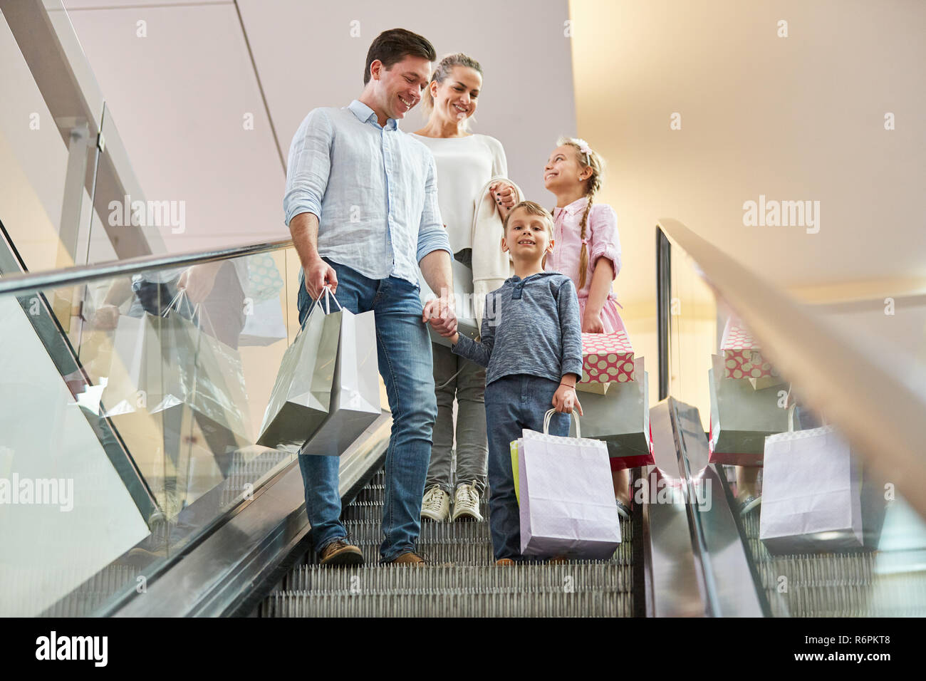 Eltern und zwei Kindern auf einer Rolltreppe mit Tüten im Einkaufszentrum Stockfoto
