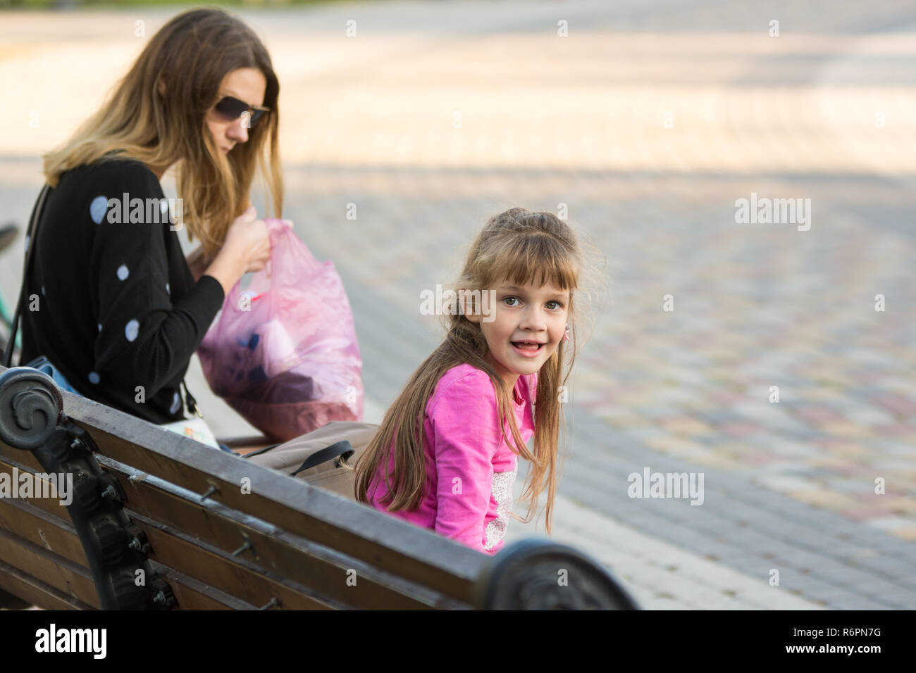 6-jähriges Mädchen und Mutter saß auf einer Bank für einen Spaziergang, das Mädchen sah mit Freude am Rahmen Stockfoto