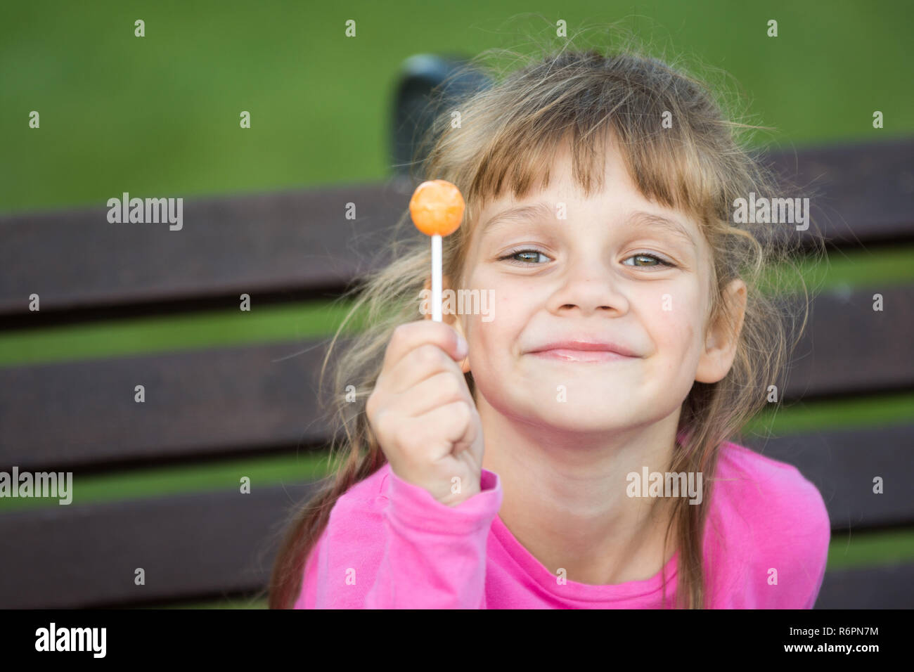 Porträt eines sechs Jahre alten fröhlichen Mädchen, hält einen Lutscher in der Hand und sieht im Rahmen zufrieden Stockfoto