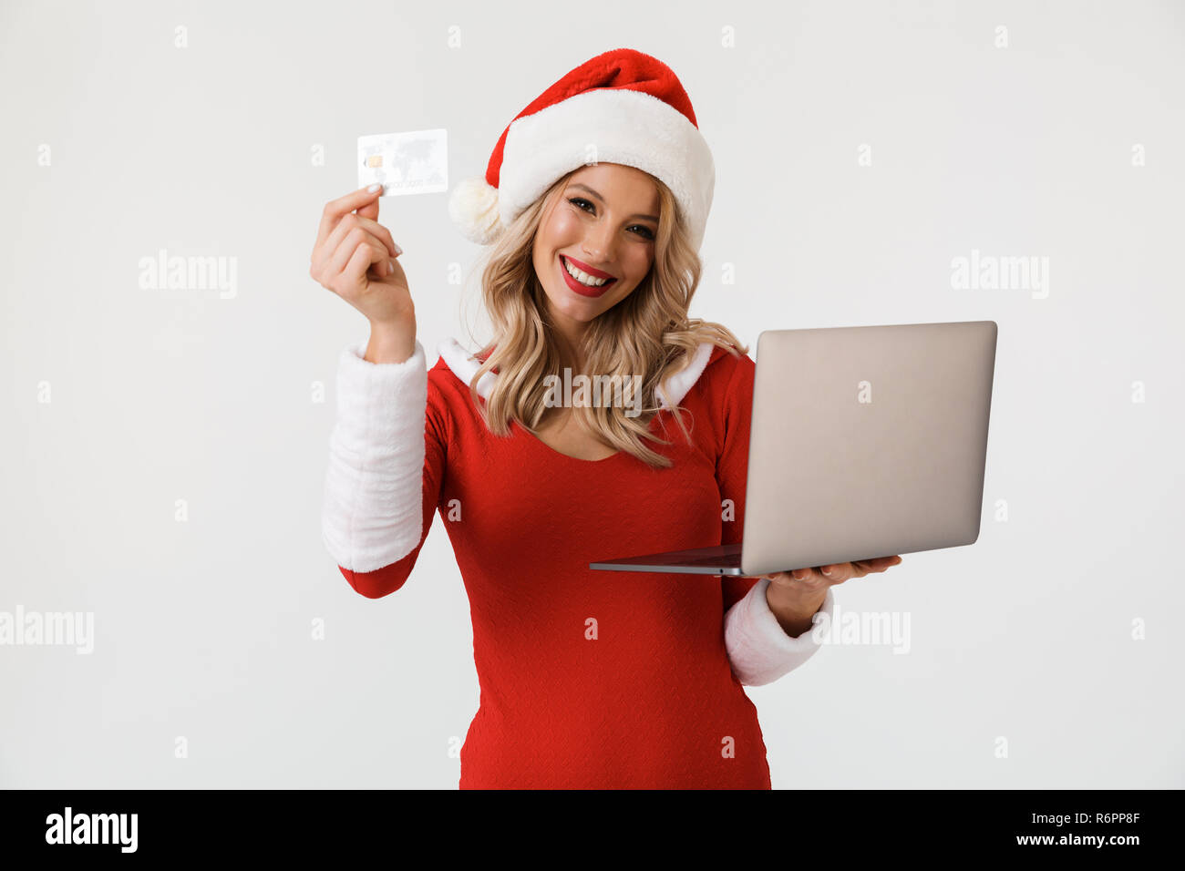 Portrait von freudiger blonde Frau in Rot neues Jahr Kostüm auf weißem Hintergrund gekleidet, mit Laptop, mit Kreditkarte Stockfoto