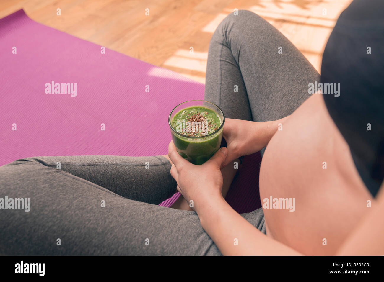 Schwangere Frau trinken gesunden grünen Smoothie sitzend auf Yoga Matte nach Übung. Gesunde Schwangerschaft Stockfoto