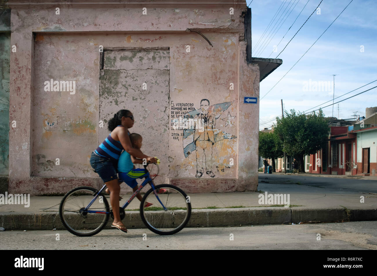 Die Frau und ihr Sohn mit dem Fahrrad vorbei an einer Wand - Malerei der Kubanischen Revolution. Cienfuegos, Kuba. Stockfoto