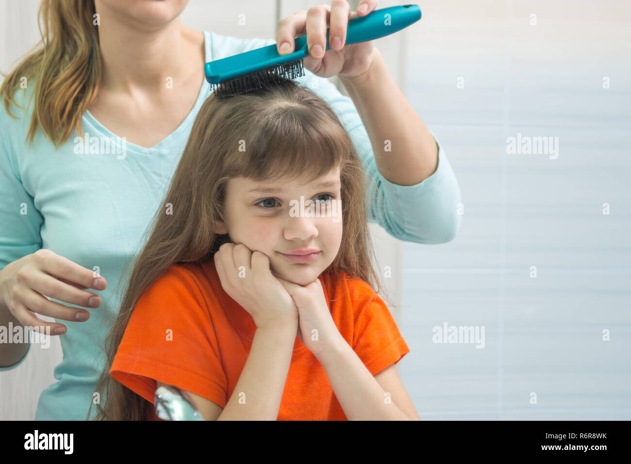Eine schöne Tochter sieht niedlich im Spiegel während Mama ihr Haar Kämme Stockfoto