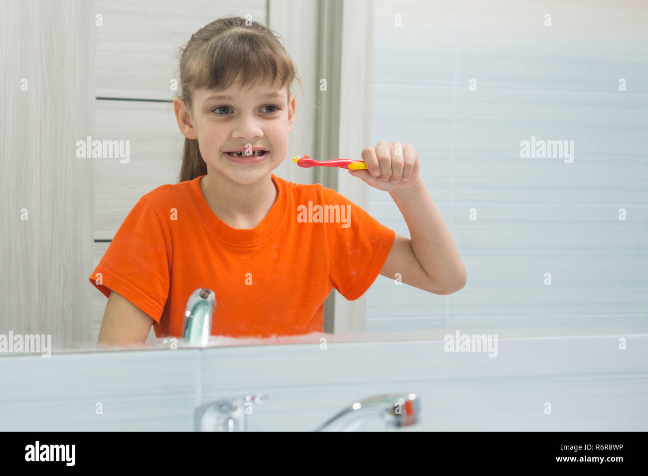 Sieben Jahre alten Mädchen sieht sich selbst im Spiegel vor dem putzen ihre Zähne Stockfoto