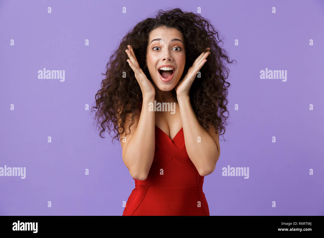 Portrait von eine aufgeregte Frau mit dunklen lockigen Haar rotes Kleid über violett Hintergrund isoliert, Erfolg feiern. Stockfoto