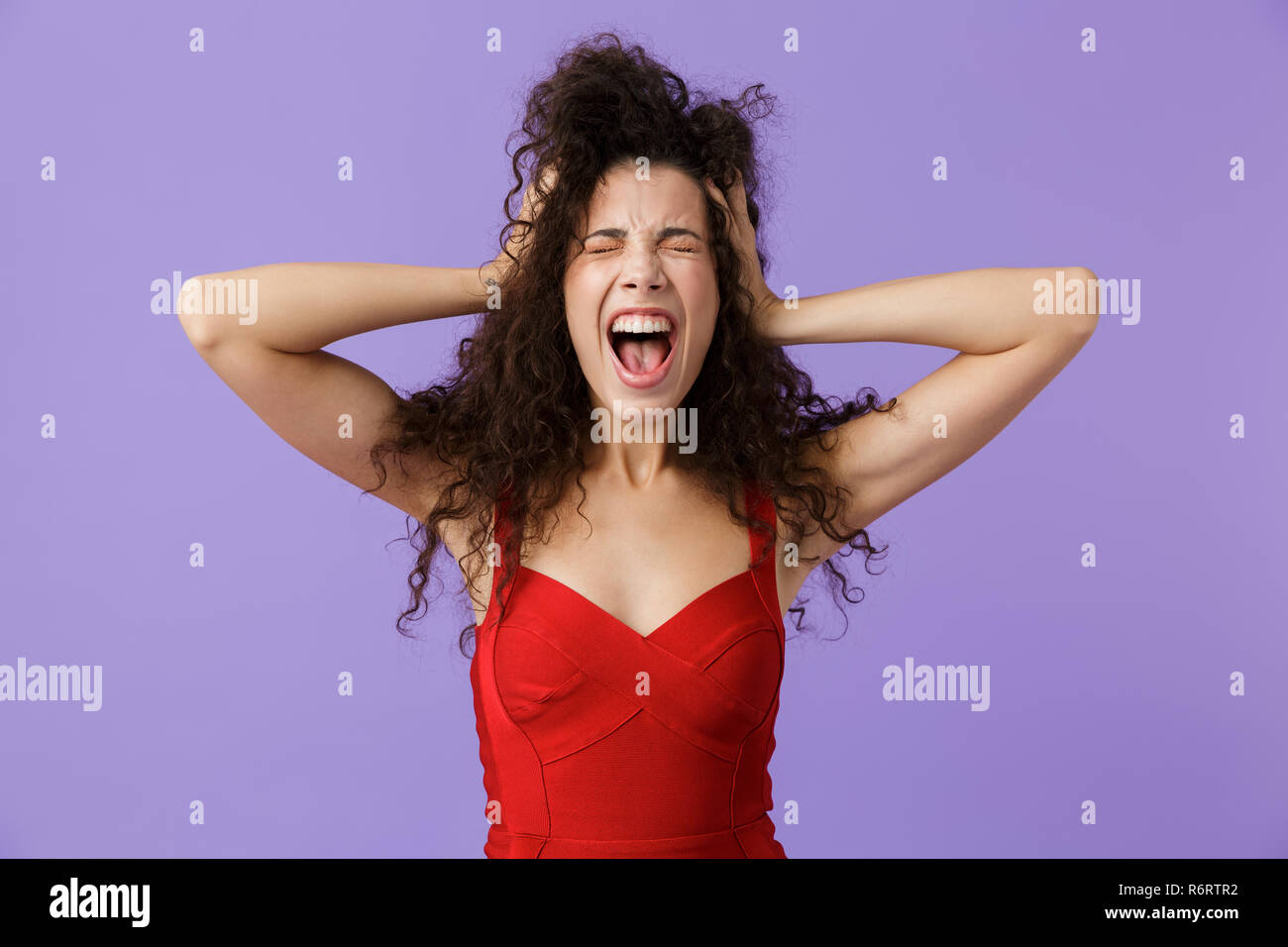 Portrait von eine wütende Frau mit dunklen lockigen Haar rotes Kleid über violett Hintergrund isoliert, schreiend laut Stockfoto