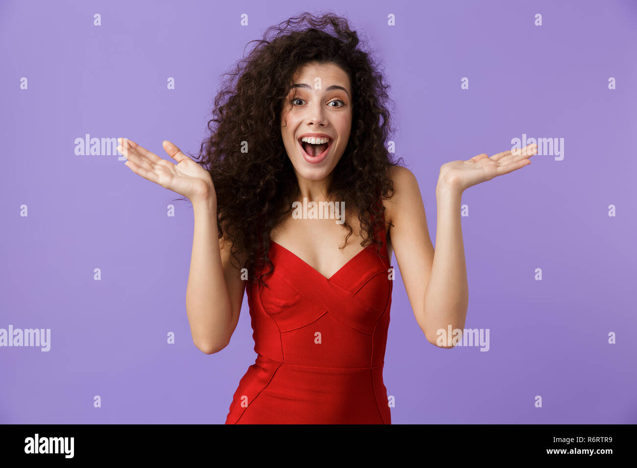 Porträt eines fröhliche Frau mit dunklen lockigen Haar rotes Kleid über violett Hintergrund isoliert, Erfolg feiern. Stockfoto