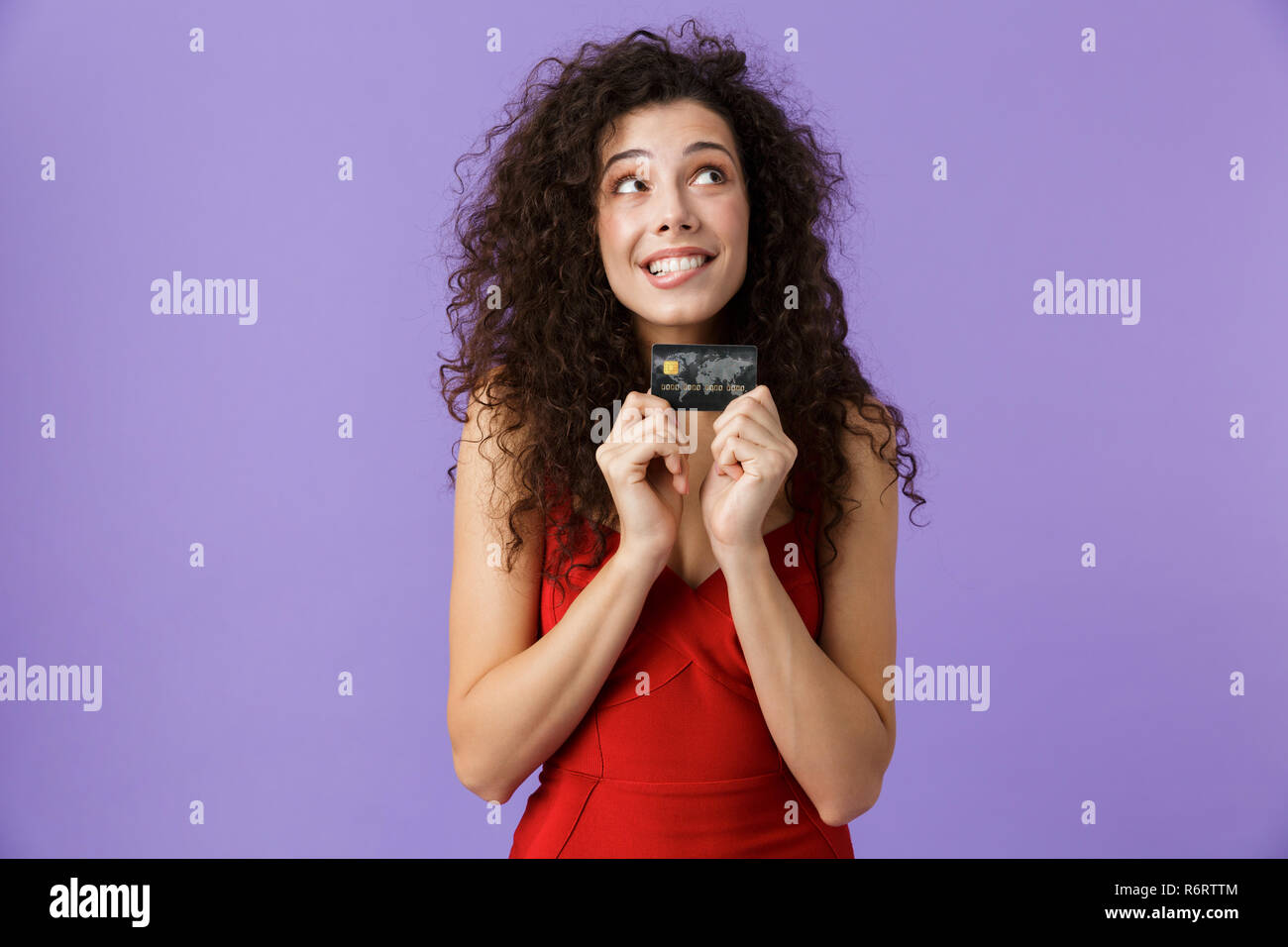 Portrait von freut sich Frau mit dunklen lockigen Haar rotes Kleid über violett Hintergrund isoliert, Kunststoff Kreditkarte Stockfoto