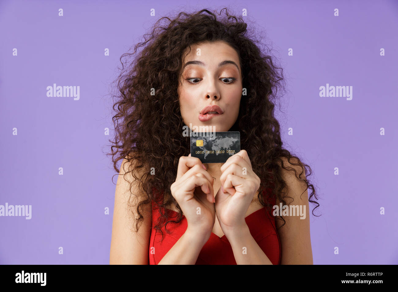 Porträt eines fröhliche Frau mit dunklen lockigen Haar rotes Kleid über violett Hintergrund isoliert, Kunststoff Kreditkarte Stockfoto