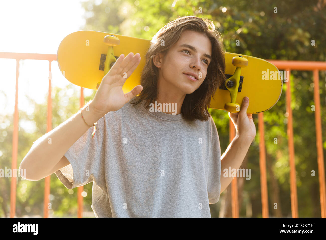 Foto von brunette Kerl 16-18 in Freizeitkleidung auf Rampe in Skate Park und halten Skateboard über die Schultern während der sonnigen Sommertag Stockfoto