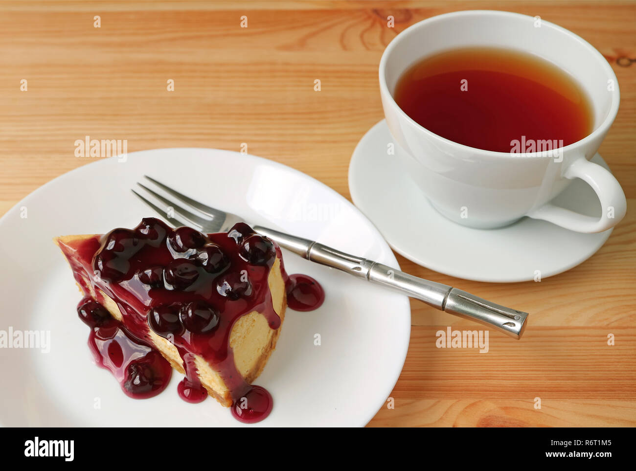 Leckere gebackene Käsetorte mit heidelbeer Sauce und eine heiße Tasse Tee serviert auf hölzernen Tisch Stockfoto