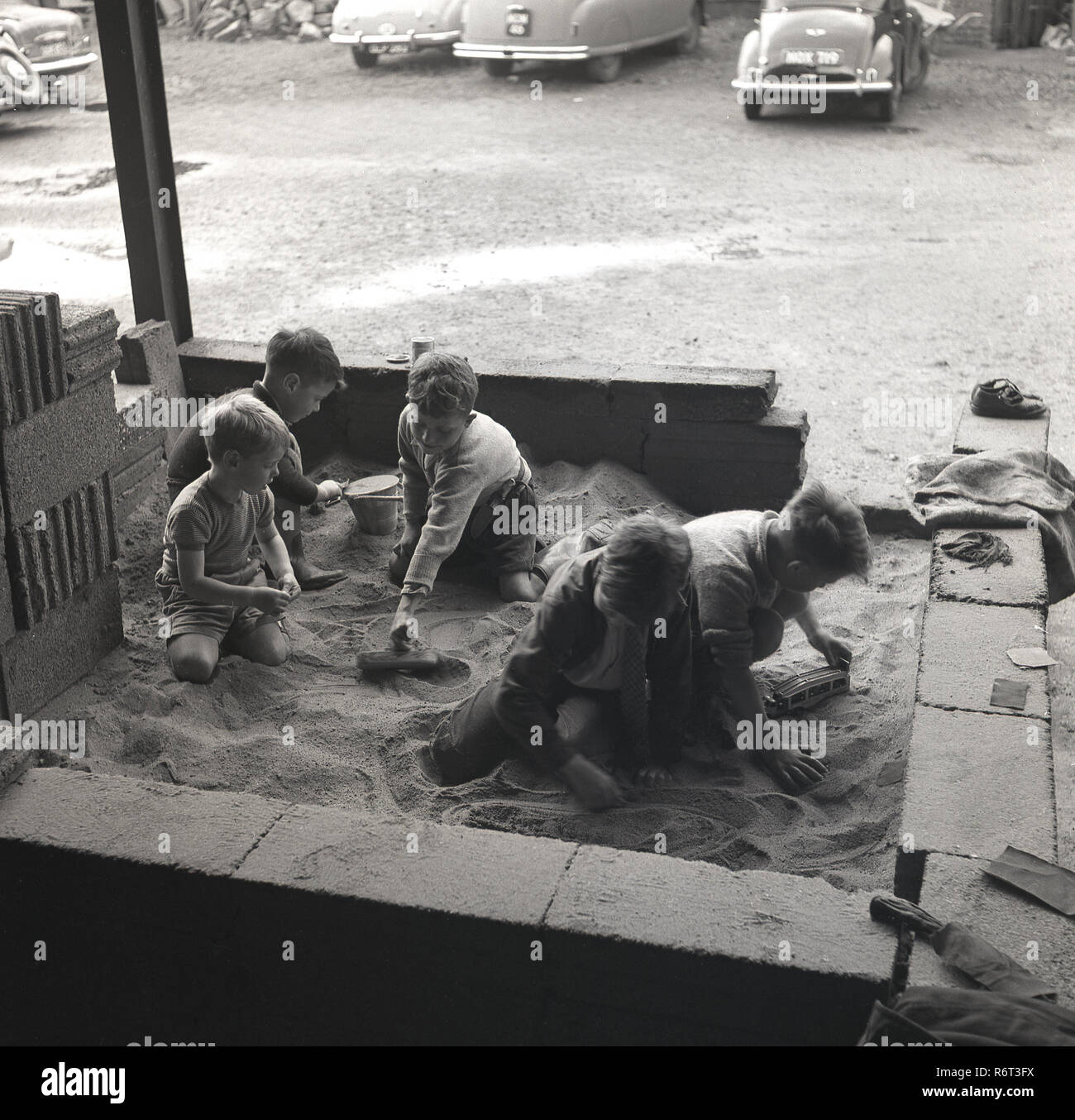 1960er Jahre, eine Gruppe von Jungen, die zusammen spielen in einem behelfsmäßigen Sandkasten draußen an einem builders Yard oder Depot, England, UK. Stockfoto