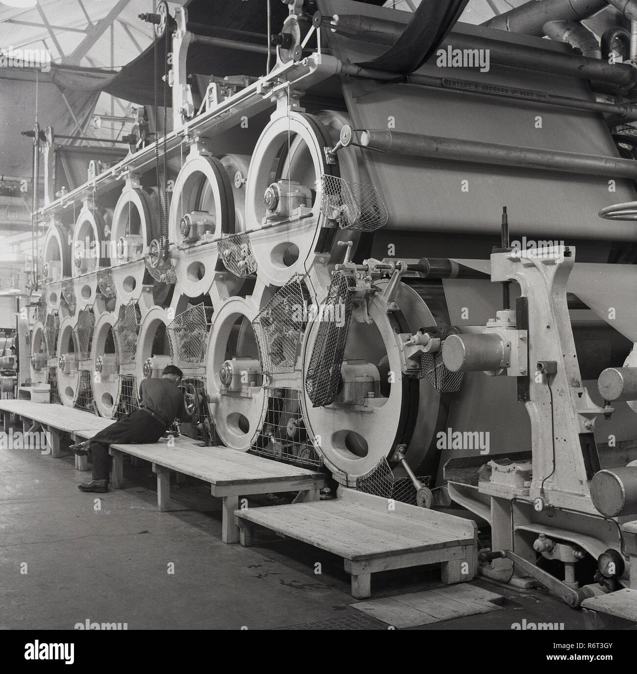 1950, historische, mann Kontrolle ein Teil auf die riesigen Maschinen zur Herstellung von Papier auf der Brittains Papierfabrik, Stoke on Trent, England, UK. Stockfoto