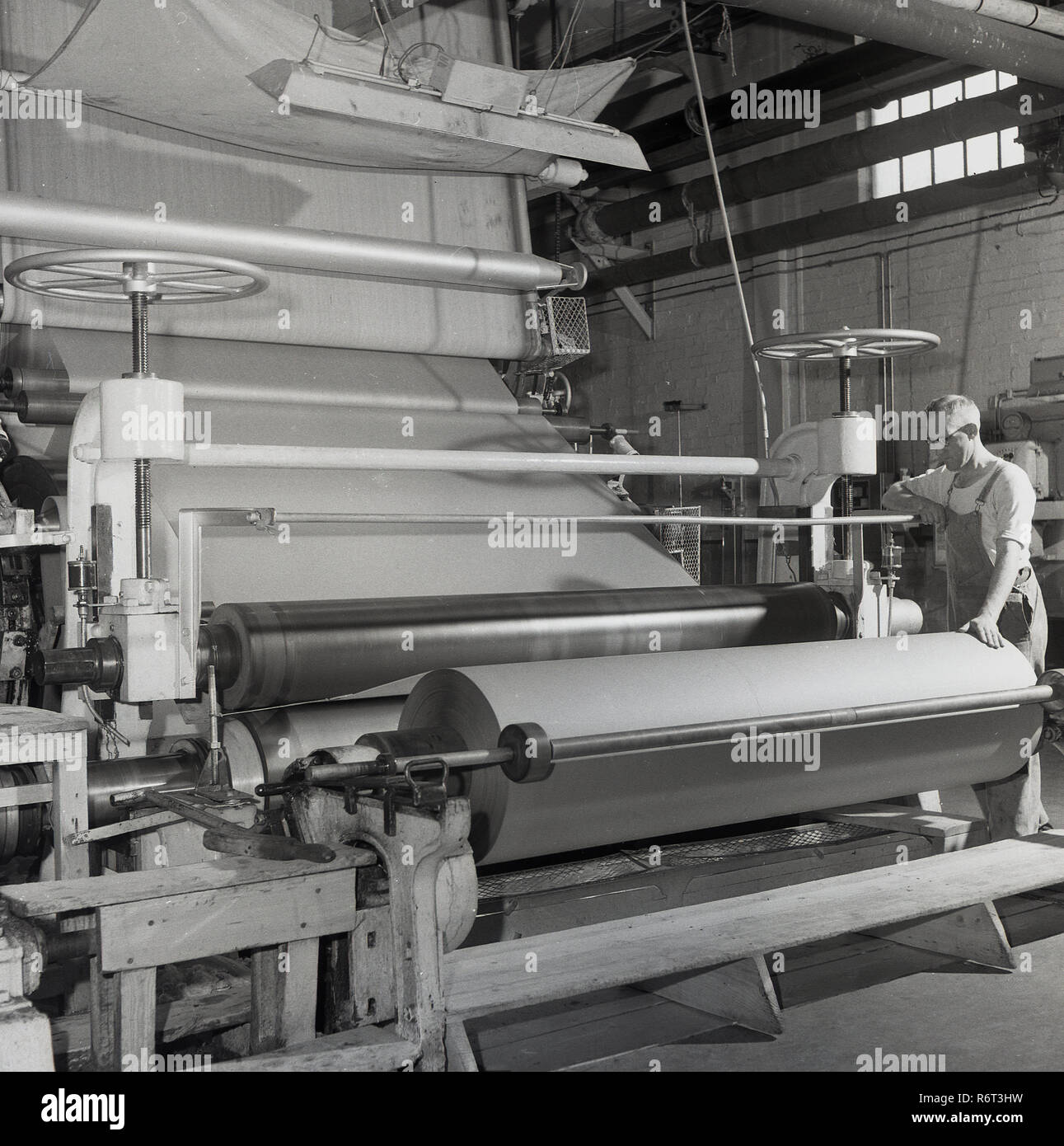1950, historische, Brittains Papierfabrik, ein männlicher Arbeiter in der Fabrik die Beaufsichtigung der Arbeiten einer großen industriellen Maschinen, eine Rolle, wo die Blätter der hergestellten Papier auf fertig sind. Stockfoto