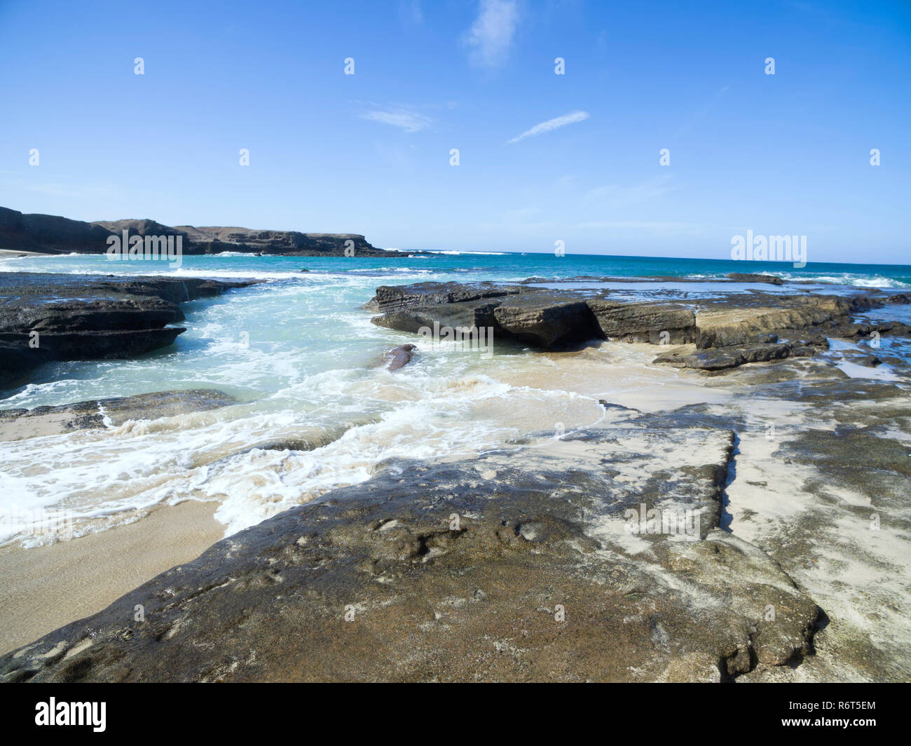 Sandstrand mit Felsen Plattformen, vulkanischen Bergen im Hintergrund, an einem sonnigen Sommertag. Stockfoto
