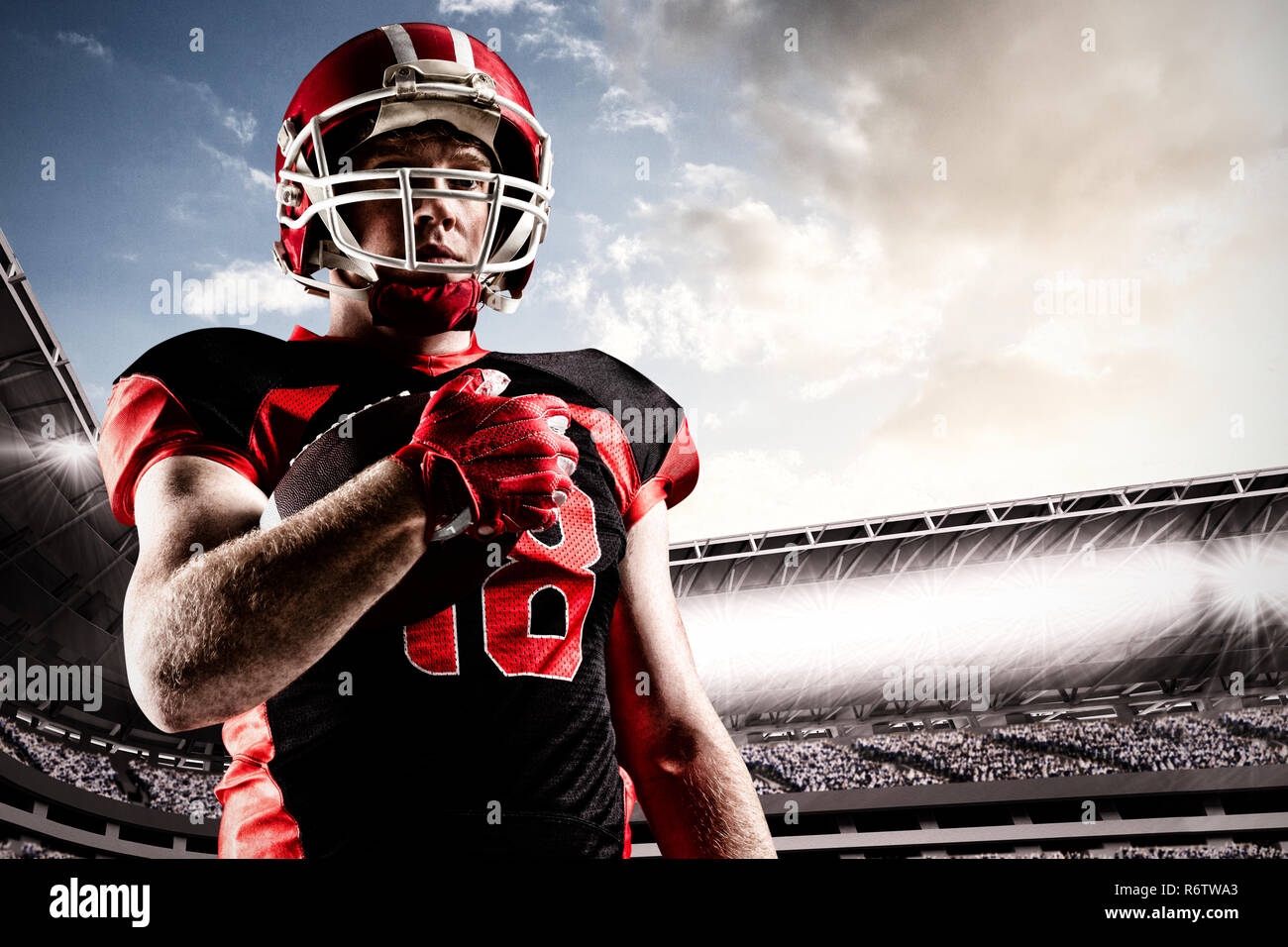 American football player im Helm Holding rugby ball gegen überfüllten Stadion mit bewölktem Himmel Stockfoto
