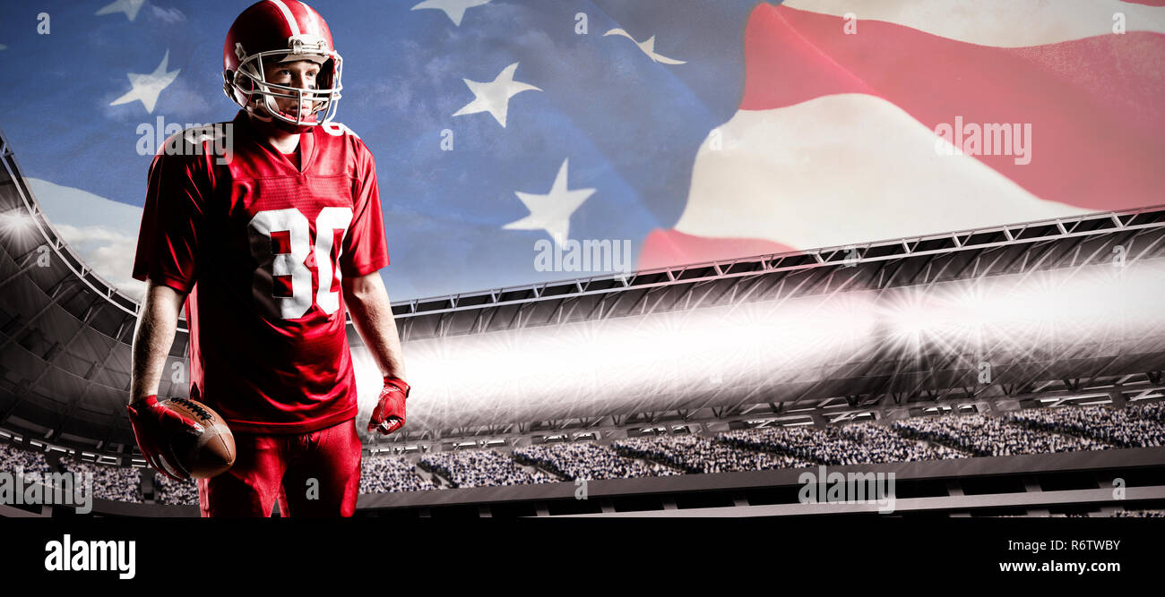American football player stehend mit rugby ball und Helm gegen die amerikanische Flagge mit Sternen und Streifen Stockfoto